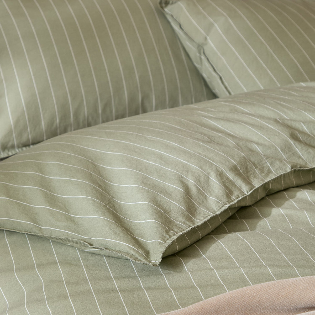 Close-up of the Linear Stripe Cotton Printed Duvet Cover Set in Forest, showing pillowcases and duvet in green cotton with fine white pinstripes.