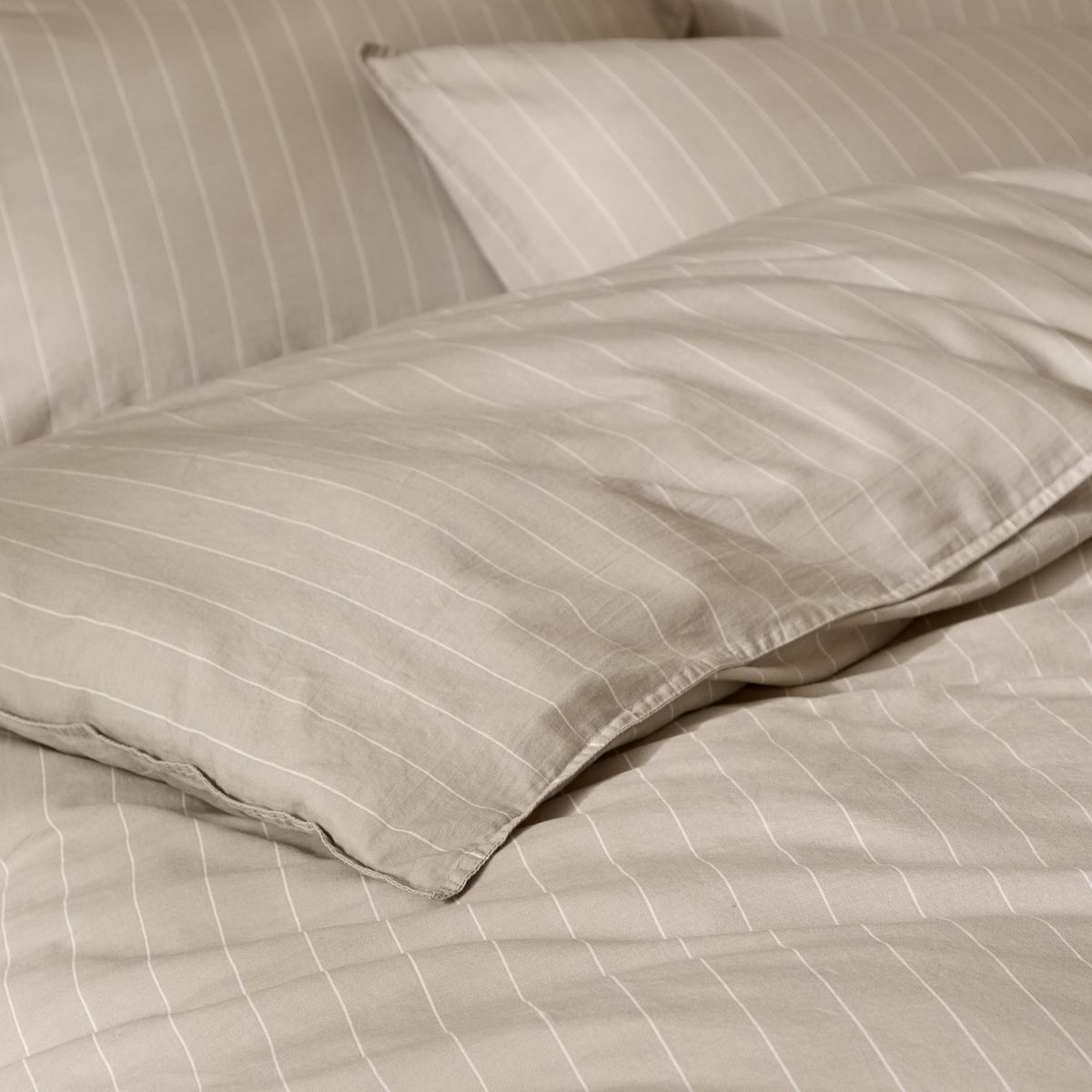 Close-up of the Linear Stripe Cotton Printed Duvet Cover Set in natural beige, showing pillowcases with fine off-white pinstripes and soft cotton folds.