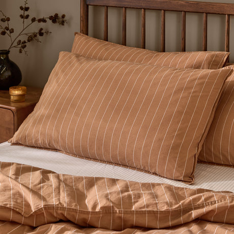 Linear Stripe Printed Cotton Pillowcase Pair in Demerara Sugar, tan with fine white pinstripes, shown styled on a bed with matching striped duvet cover in a bedroom setting.