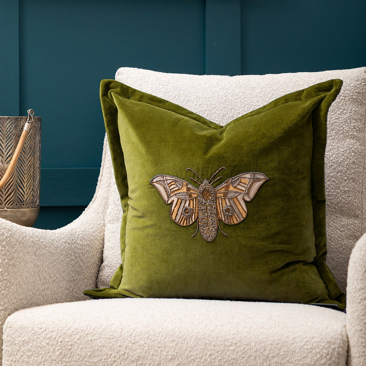 Luna Animal Velvet Cushion in olive green, square with beaded moth embroidery in cream and metallic thread, styled on a cream boucle armchair.