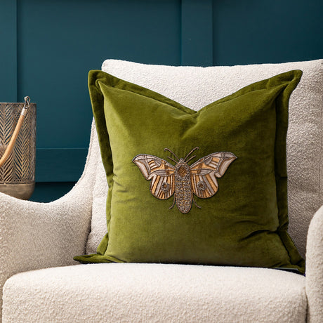Luna Animal Velvet Cushion in olive green, square with beaded moth embroidery in cream and metallic thread, styled on a cream boucle armchair.