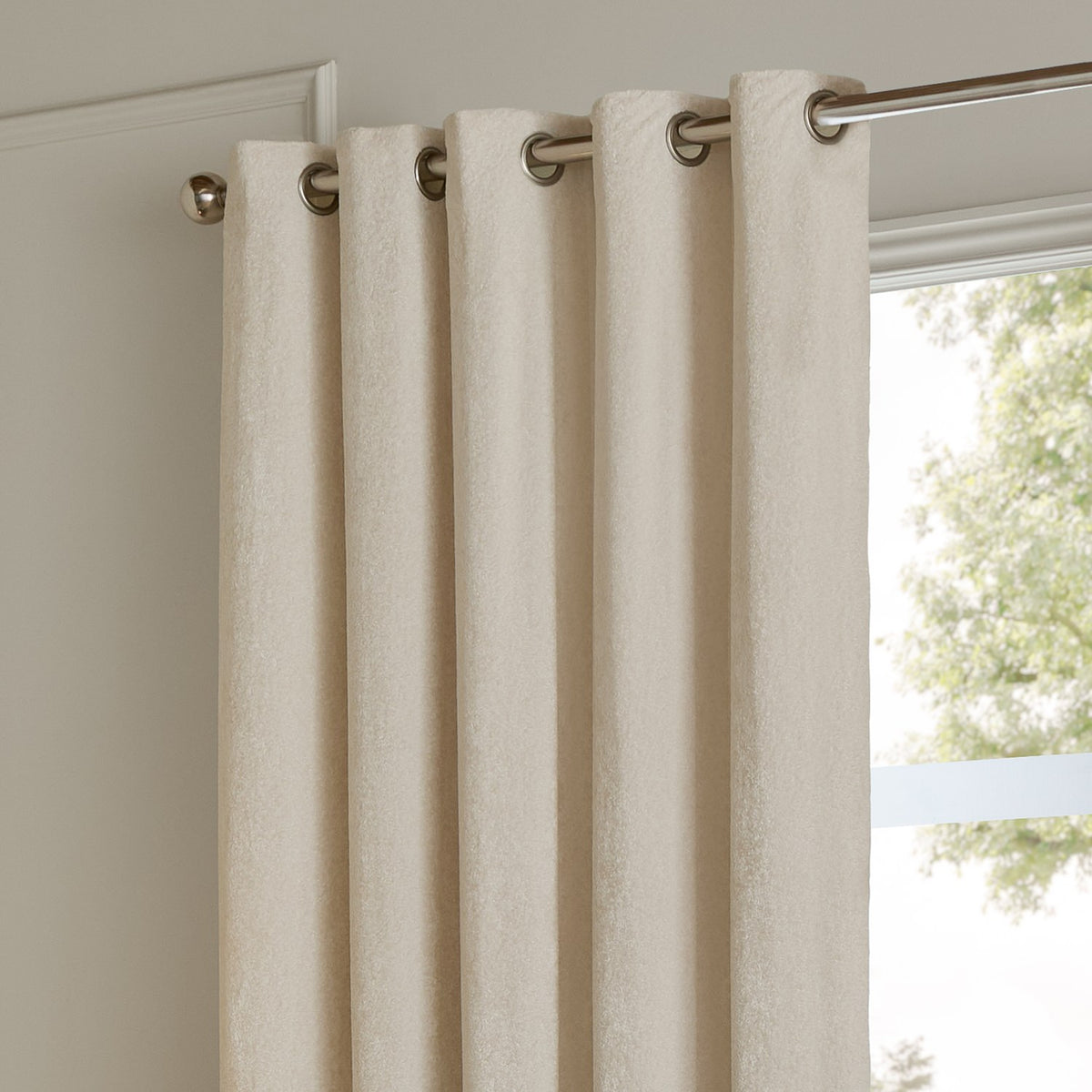 Ivory velvet eyelet curtains with brushed metal grommets hanging from a chrome pole beside a window, showing fully lined fabric with a soft sheen.