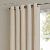 Ivory velvet eyelet curtains with brushed metal grommets hanging from a chrome pole beside a window, showing fully lined fabric with a soft sheen.