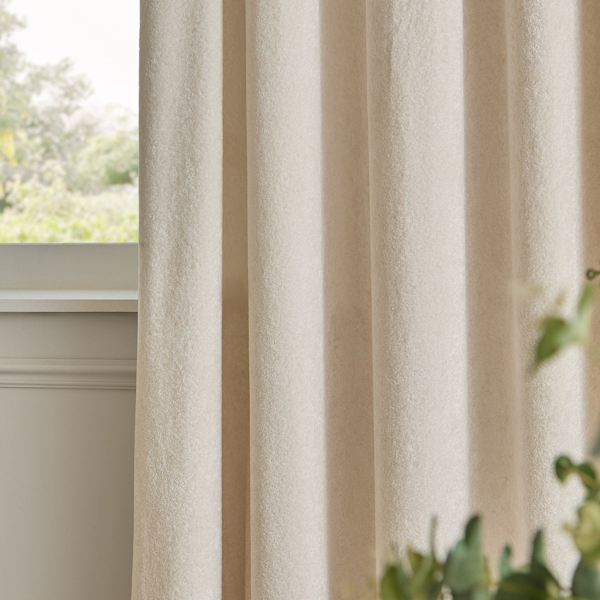 Ivory Lustre Velvet eyelet curtains shown in soft folds by a window, fully lined fabric with a subtle sheen and even drape.