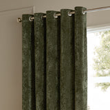 Lustre Velvet Plain Fully Lined Eyelet Curtains in malachite green, hung on a chrome pole with visible grommets, shown against a wall beside a window.