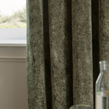 Lustre Velvet eyelet curtains in malachite green, showing the crushed pile texture and heavy folds, hung beside a window with a light interior setting.