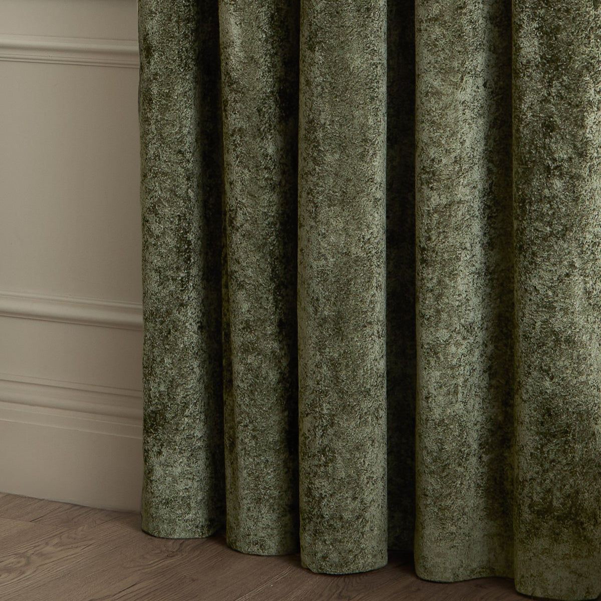 Close-up of Lustre Velvet Plain Fully Lined Eyelet Curtains in Malachite Green, showing draped folds of crushed velvet fabric against a light wall.