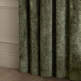Close-up of Lustre Velvet Plain Fully Lined Eyelet Curtains in Malachite Green, showing draped folds of crushed velvet fabric against a light wall.
