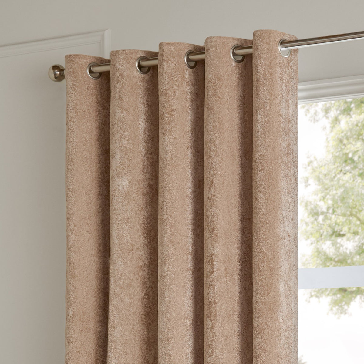 Lustre Velvet Plain Fully Lined Eyelet Curtains in oyster, showing chrome eyelets on a metal rail against a light wall near a window.