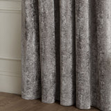 Close-up of Lustre Velvet Plain Fully Lined Eyelet Curtains in pewter grey, showing crushed velvet fabric with soft folds against a panelled wall and wooden floor.