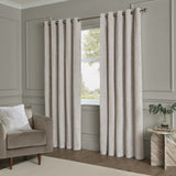 Lustre Velvet Plain Fully Lined Eyelet Curtains in silver, shown floor-length on a bronze pole in a grey-panelled living room beside a mink armchair and marble side table.