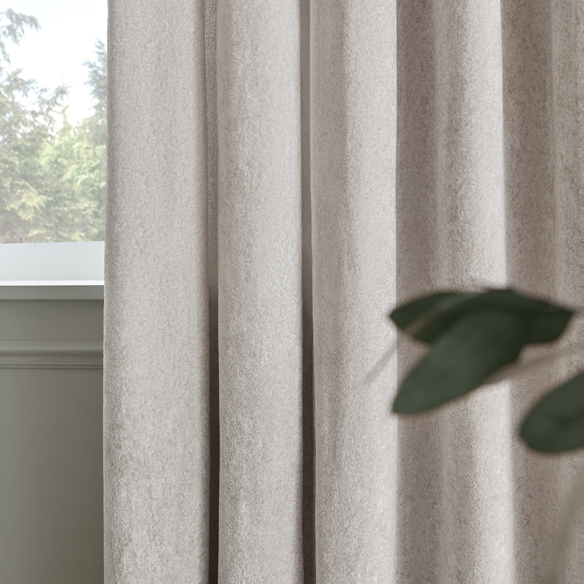 Lustre Velvet Plain Fully Lined Eyelet Curtains in silver, shown in soft folds by a window, with a woven velvet texture and low sheen finish.