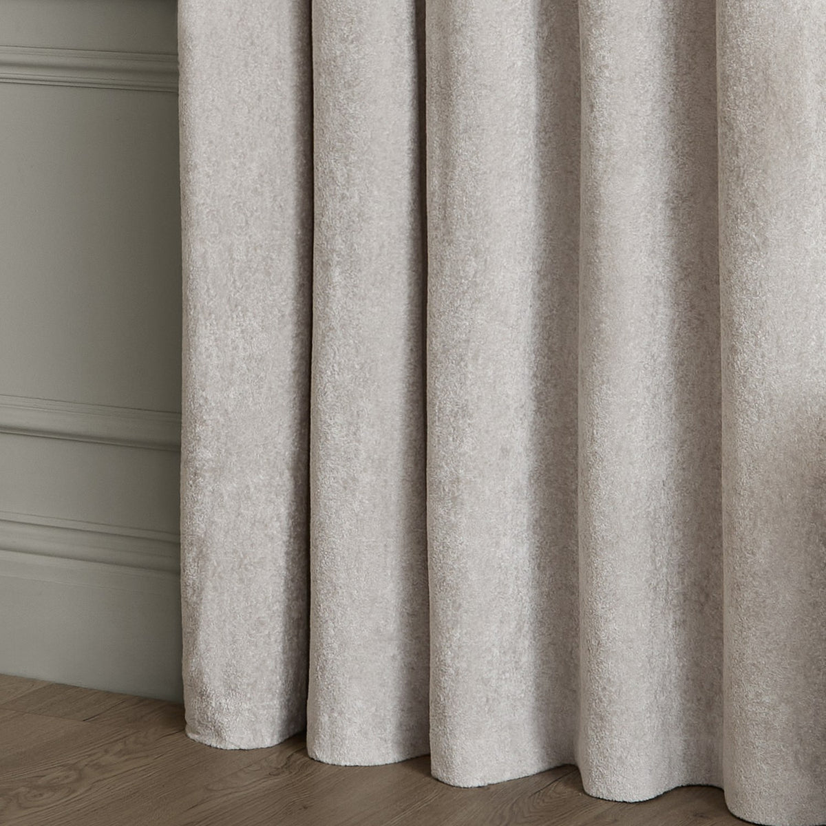 Lustre Velvet Plain Fully Lined Eyelet Curtains in silver, shown in soft folds with a subtle sheen against a panelled wall and wooden floor.