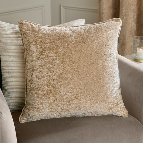 Square Lustre Velvet cushion in champagne, showing crushed velvet pile with piped edges, styled on a sofa with a striped cushion and curtain in the background.