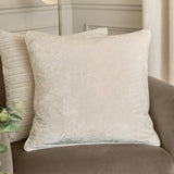 Lustre Velvet Plain Polyester Cushion in ivory, a square crushed-velvet cushion with piped edges, shown on a brown sofa in a living room setting.