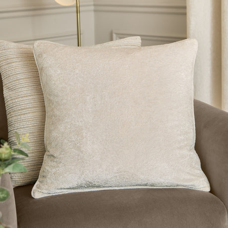 Lustre Velvet Plain Polyester Cushion in ivory, a square crushed-velvet cushion with piped edges, shown on a brown sofa in a living room setting.
