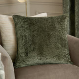 Lustre Velvet Plain Polyester Cushion in Malachite Green, a square crushed-velvet cushion with self-piped edge, shown on a taupe armchair beside a striped cream cushion.
