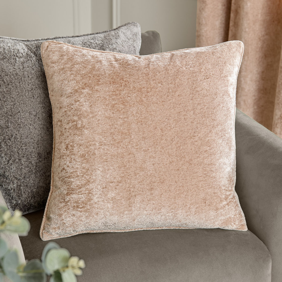 Square Lustre Velvet cushion in oyster beige with self-piped edges, shown on a grey sofa beside curtains in a living room setting.