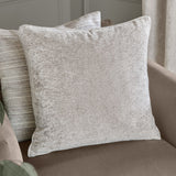 Lustre Velvet Plain Polyester Cushion in silver with a crushed-velvet sheen, square shape and piped edge, styled on a sofa with a striped cushion behind.