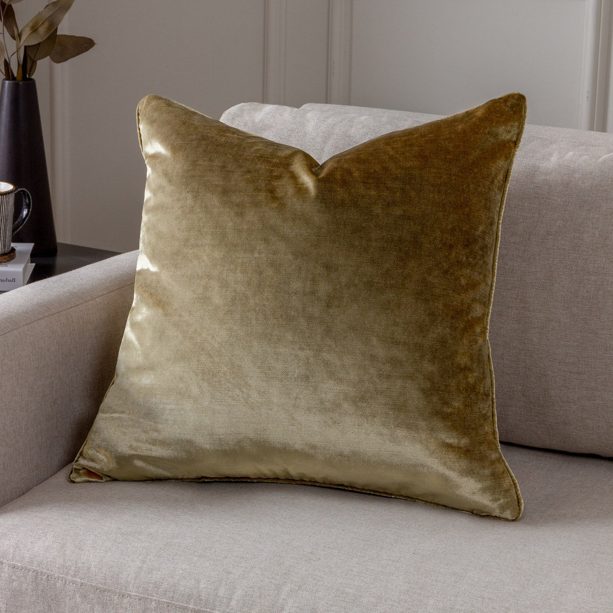 Luxe Velvet Plain Polyester Cushion in gold, a square velvet-feel cover with piped edges, shown on a light grey sofa in a living room setting.