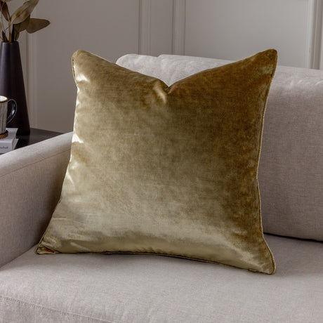 Luxe Velvet Plain Polyester Cushion in gold, a square velvet-feel cover with piped edges, shown on a light grey sofa in a living room setting.
