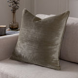Luxe Velvet Plain Polyester Cushion in mink, a square scatter cushion with piped edges shown on a neutral sofa beside a vase and books.