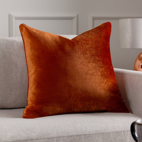 Luxe Velvet Plain Polyester Cushion in rust, a square burnt-orange velvet-feel cushion with soft sheen, shown propped on a light grey sofa in a living room setting.