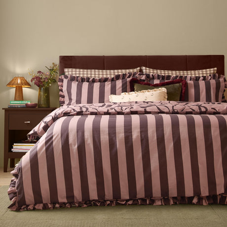 La Vie En Bows reversible duvet cover set in mocha and aubergine stripe with ruffled edge trim, styled on a bed with matching pillowcases in a bedroom setting.