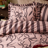 La Vie En Bows reversible duvet cover set in mocha, showing bow print and striped sides with frilled-edge pillowcase on a bed.
