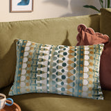 Metro Abstract Jacquard Velvet Cushion in multicoloured green, teal and amber geometric pattern, shown on an olive-green sofa beside a rust pink cushion.