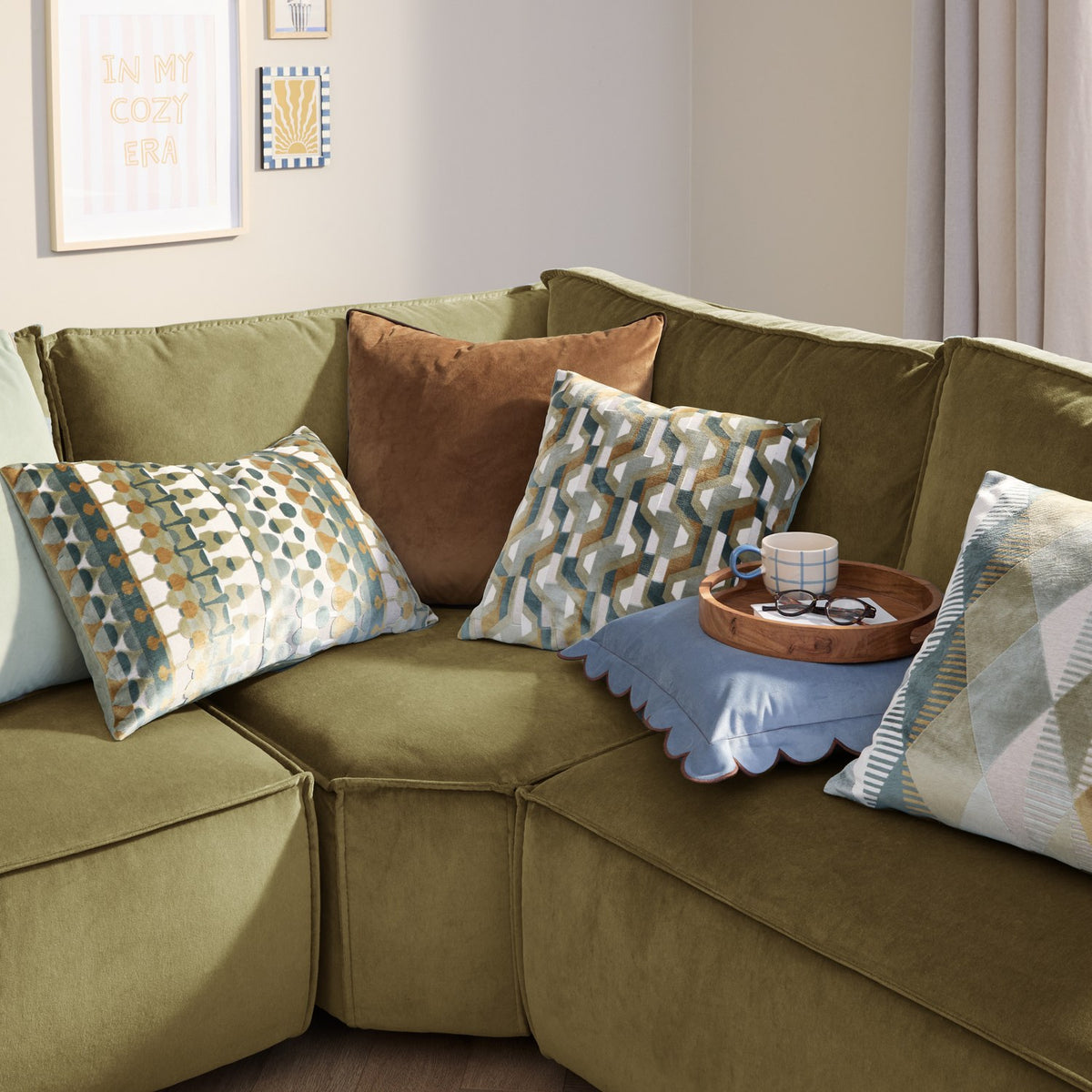 Metro Abstract Jacquard Velvet Cushion in green, teal, amber and cream geometric pattern, styled on an olive green sofa with coordinating cushions.