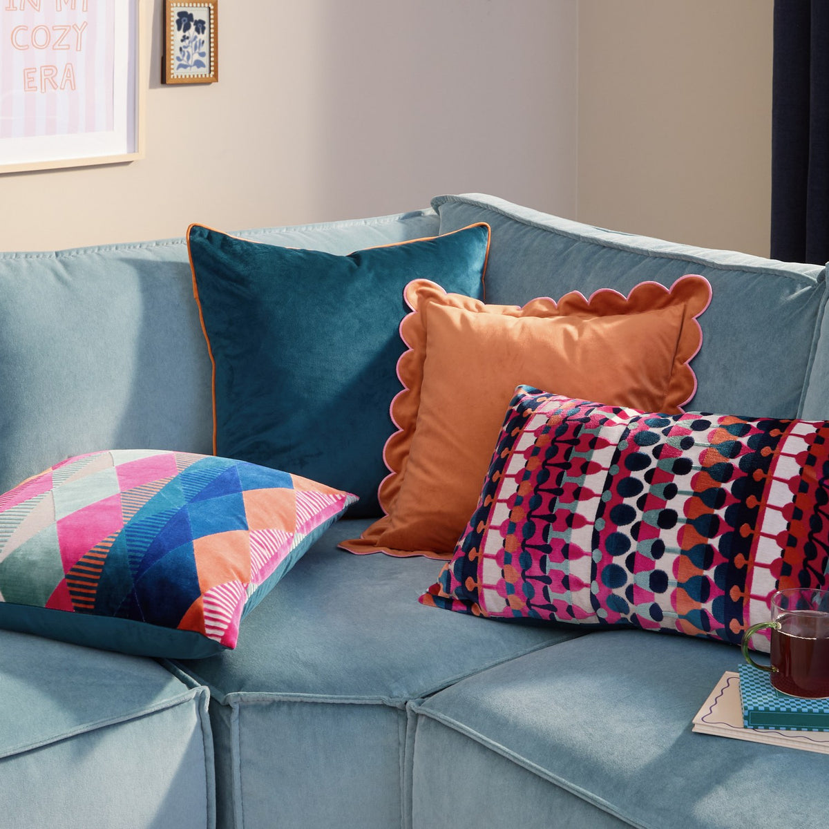 Metro Abstract Jacquard Velvet Cushion in multicoloured geometric print, styled on a blue velvet sofa alongside teal, orange and patterned scatter cushions.