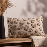 Maeve Animal Cotton Cushion in natural, a rectangular bolster with raised tonal leopard-print tufts, shown on a wooden bench beside dried grasses and a woven throw.