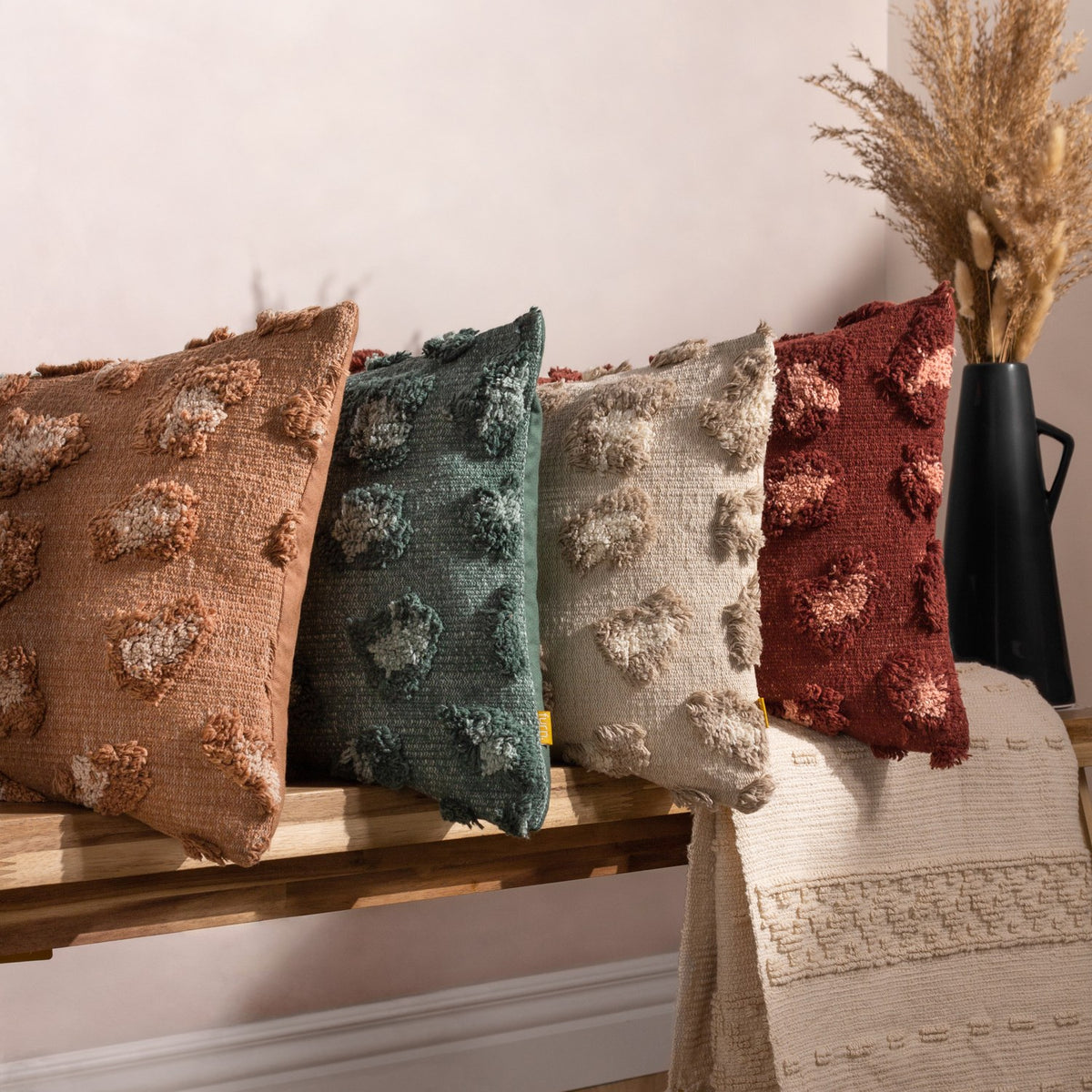 Maeve Animal Cotton Cushion in natural, styled with coordinating tufted leopard-print cushions in terracotta, teal, beige and burgundy on a wooden bench with a woven throw.