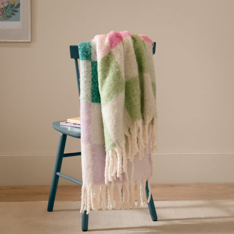 Maisie Check Polyester Throw in Aqua Blossom, a fringed multicolour check blanket in lilac, teal, cream, pink and green, draped over a teal chair in a living room.