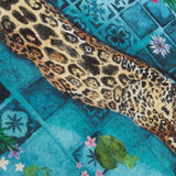 Majorelle reversible polyester cushion in azure, close-up of a hand-painted leopard print over blue Moroccan tile pattern with palm fronds and tropical flowers.