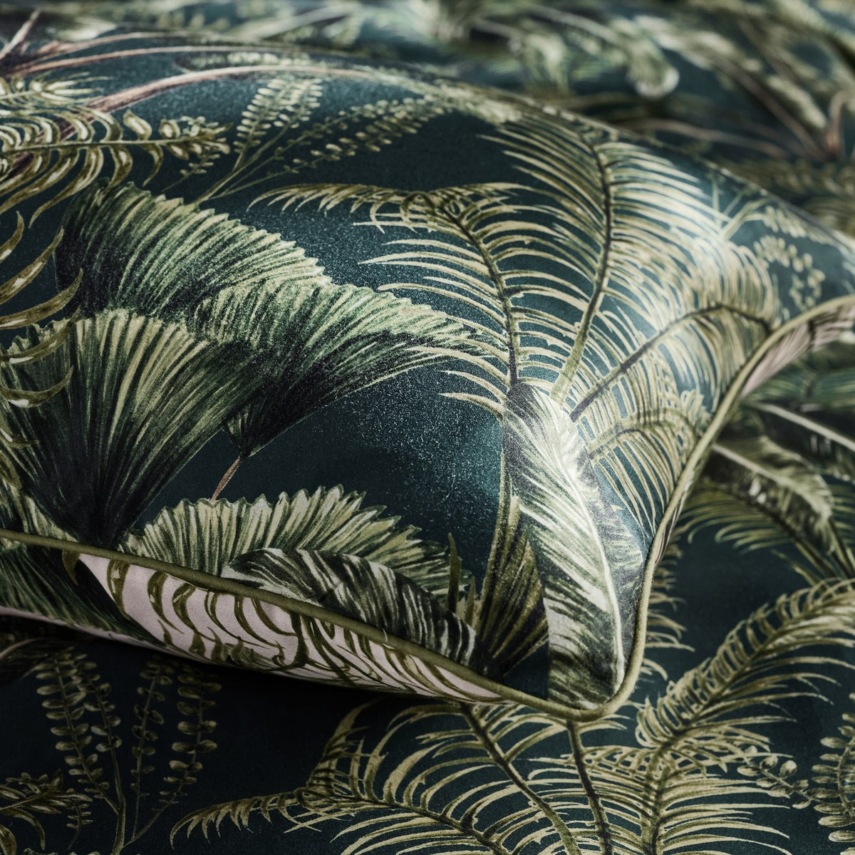 Close-up of the Majorelle Cotton Duvet Cover Set in green, showing a tropical palm and fern print with cord-piped edge trim and reversible pale underside.