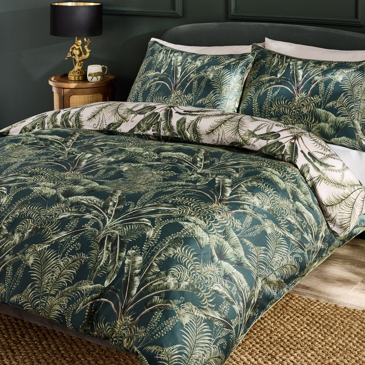 Majorelle Cotton Leaf Duvet Cover Set in green, styled on a bed with matching pillowcases featuring a tropical palm and fern print, shown in a dark bedroom setting.