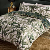 Majorelle Cotton Leaf Duvet Cover Set in green, shown on a bed with matching pillowcases in a tropical palm and fern print against a pale ground, styled in a bedroom setting.