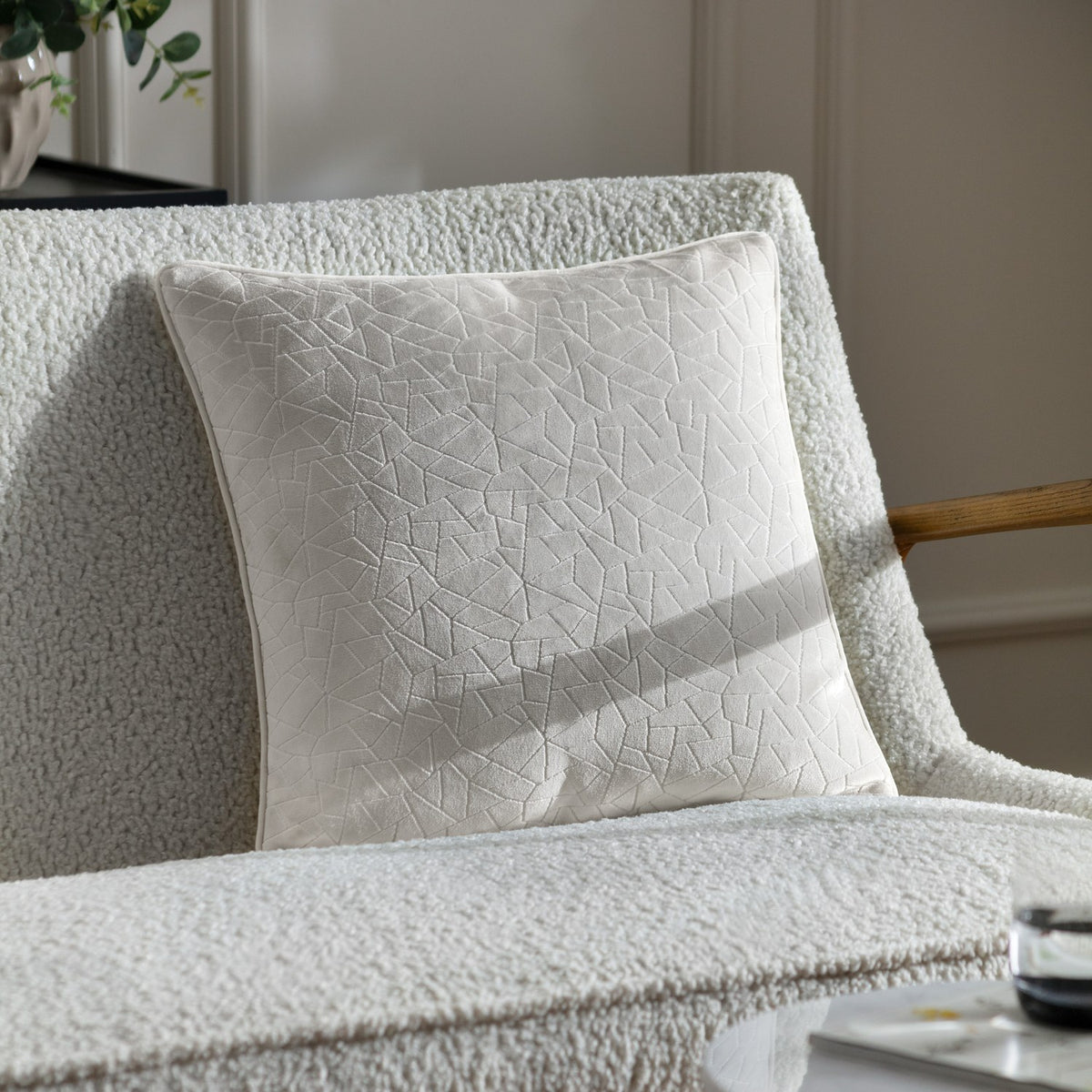 Malans Geometric Velvet Cushion in milk cream with a crackled-glass textured pattern, shown on a white bouclé sofa in a living room setting.