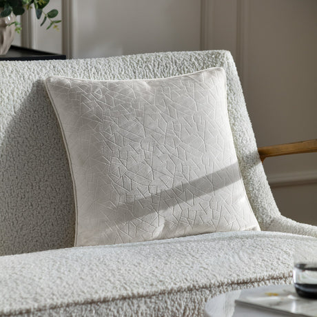 Malans Geometric Velvet Cushion in milk cream with a crackled-glass textured pattern, shown on a white bouclé sofa in a living room setting.