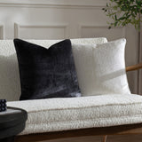 Malans Geometric Velvet Cushion in milk cream with a crackled-glass textured pattern, shown beside a black version on a cream boucle sofa.