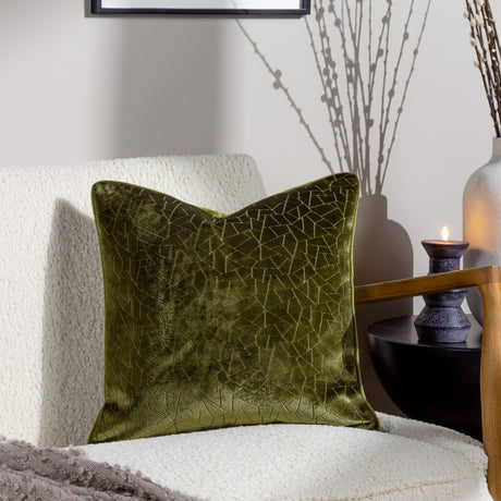 Malans Geometric Velvet Cushion in olive with piped edge, styled on a cream boucle armchair beside a candle and dried branches in a living room setting.
