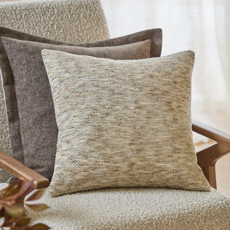 Malvern Jacquard Chenille Cushion in Griege, a 45 x 45cm square cushion with a textured, mottled weave, styled on an armchair with a brown cushion behind it.