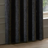 Manhattan Velvet Fully Lined Eyelet Curtains in charcoal, showing textured geometric cut-pile fabric with eyelet heading, draped floor-length beside a window in a living room setting.