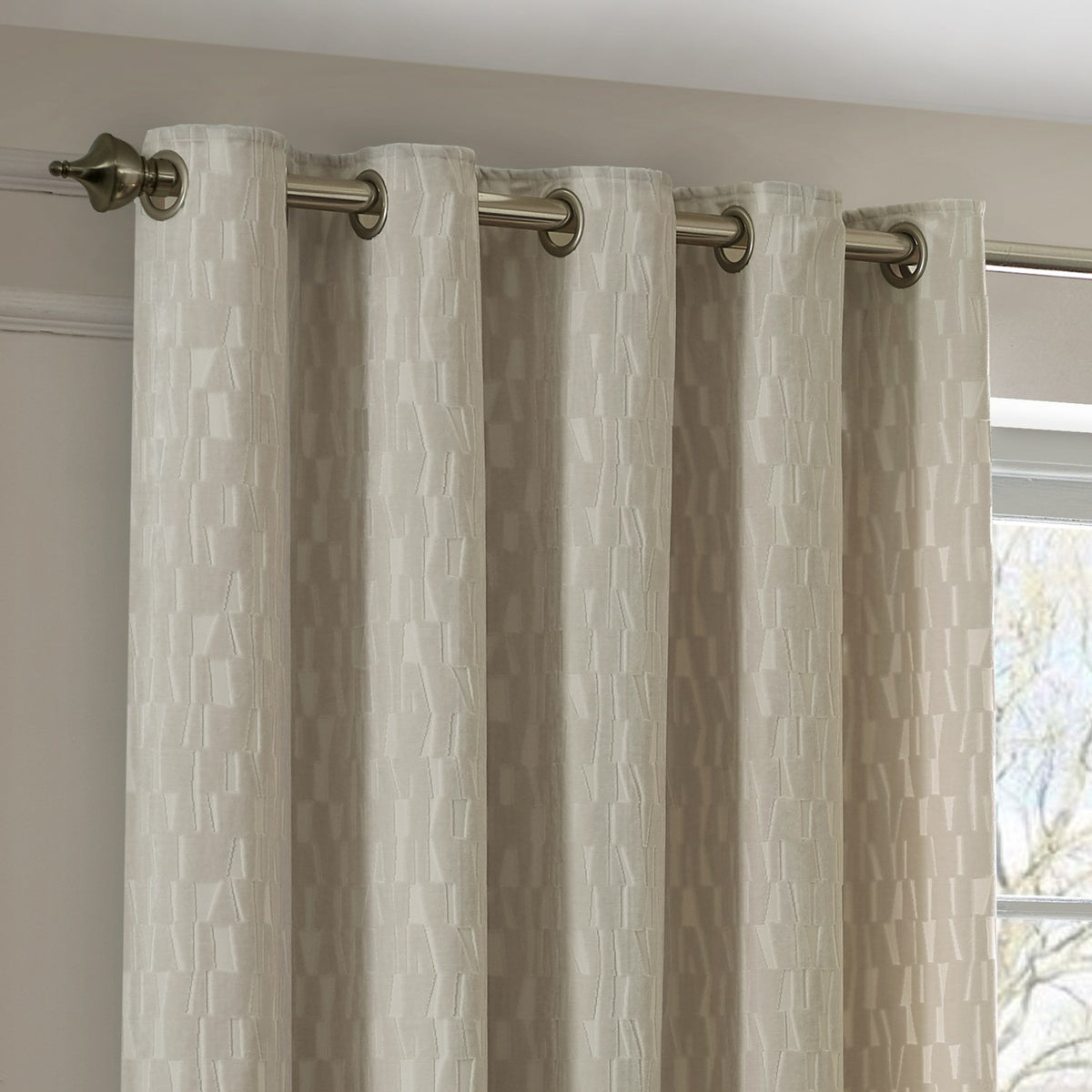 Manhattan Velvet Fully Lined Eyelet Curtains in ivory, shown on a brushed metal pole with eyelet header, textured geometric weave visible on the fabric drop.