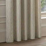 Manhattan Velvet Fully Lined Eyelet Curtains in ivory, shown hanging beside a window with soft folds highlighting the textured geometric pattern on the fabric.