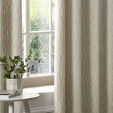 Manhattan fully lined eyelet curtains in ivory cut velvet with a textured geometric block pattern, shown hanging beside a window in a living room setting.