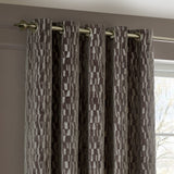 Manhattan Velvet Fully Lined Eyelet Curtains in mink brown with a textured geometric cut-velvet pattern, brass eyelets on a metal pole in a living room setting.