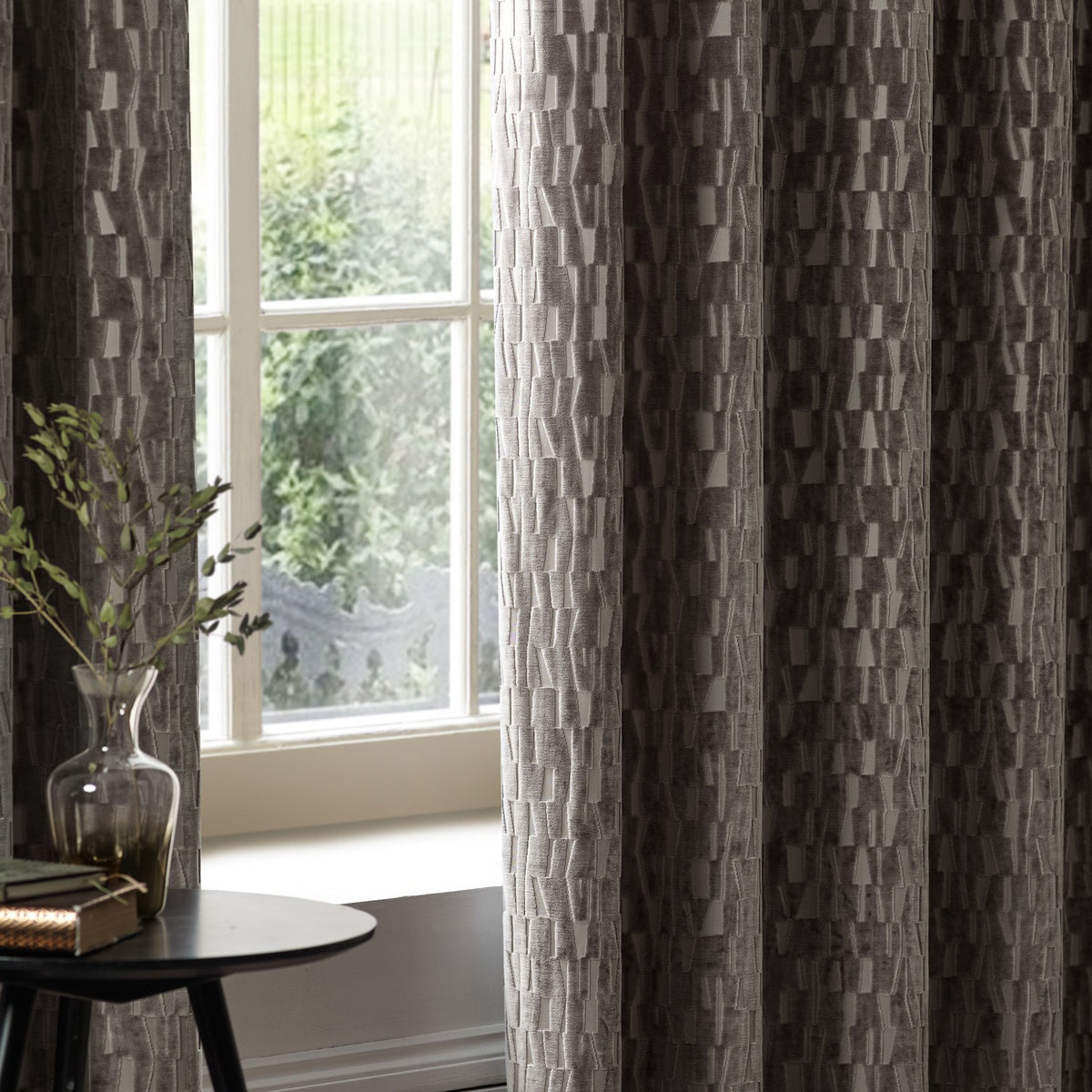 Manhattan Velvet Fully Lined Eyelet Curtains in mink brown with textured geometric pattern, shown hanging by a window in a living room setting.